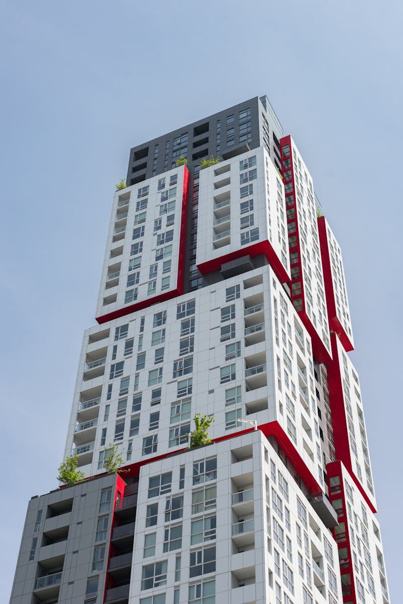 Unique architectural design of a skyscraper with striking red accents against clear sky.